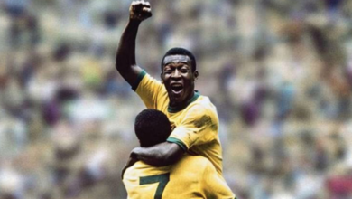 Na foto está o mineiro Pelé, um jogador negro que comemora o seu gol com o punho fechado e o braço levantado. Ele está vestido uma camisa amarela e está sendo segurado por Jairzinho, um outro jogador negro que veste uma camisa amarela com o número 7 escrito em verde nas costas.