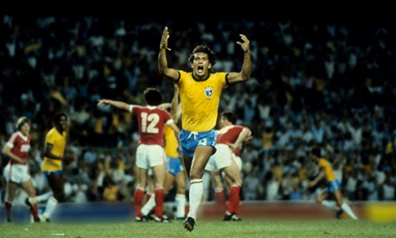 Na foto está um homem branco, com uma camisa amarela, shorts azuis e meiões brancos. Ele esta um pouco abaixado, indo em direção a uma bola de futebol branca, com detalhes triangulares pretos. Ele está em um gramado verde com uma enorme torcida atrás. Este é o mineiro Éder Aleixo.