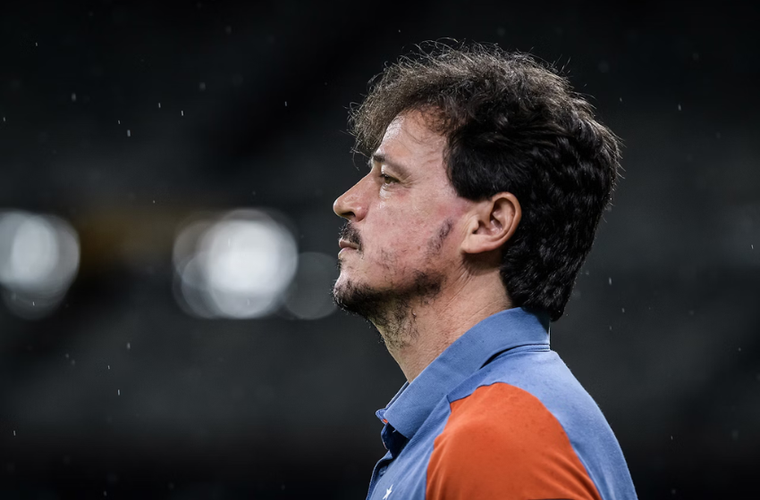 Na foto vemos Fernando Diniz, um homem branco, de barba preta e cabelo preto. Ele está usando uma camisa azul abotoada, com as mangas em cor vermelha.