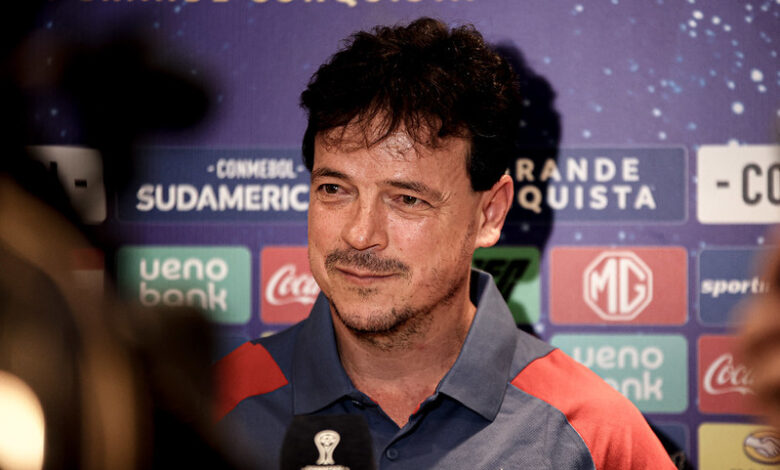 Na foto vemos Fernando Diniz, um homem branco, de barba preta e cabelo preto. Ele está usando uma camisa azul abotoada, com as mangas em cor vermelha.